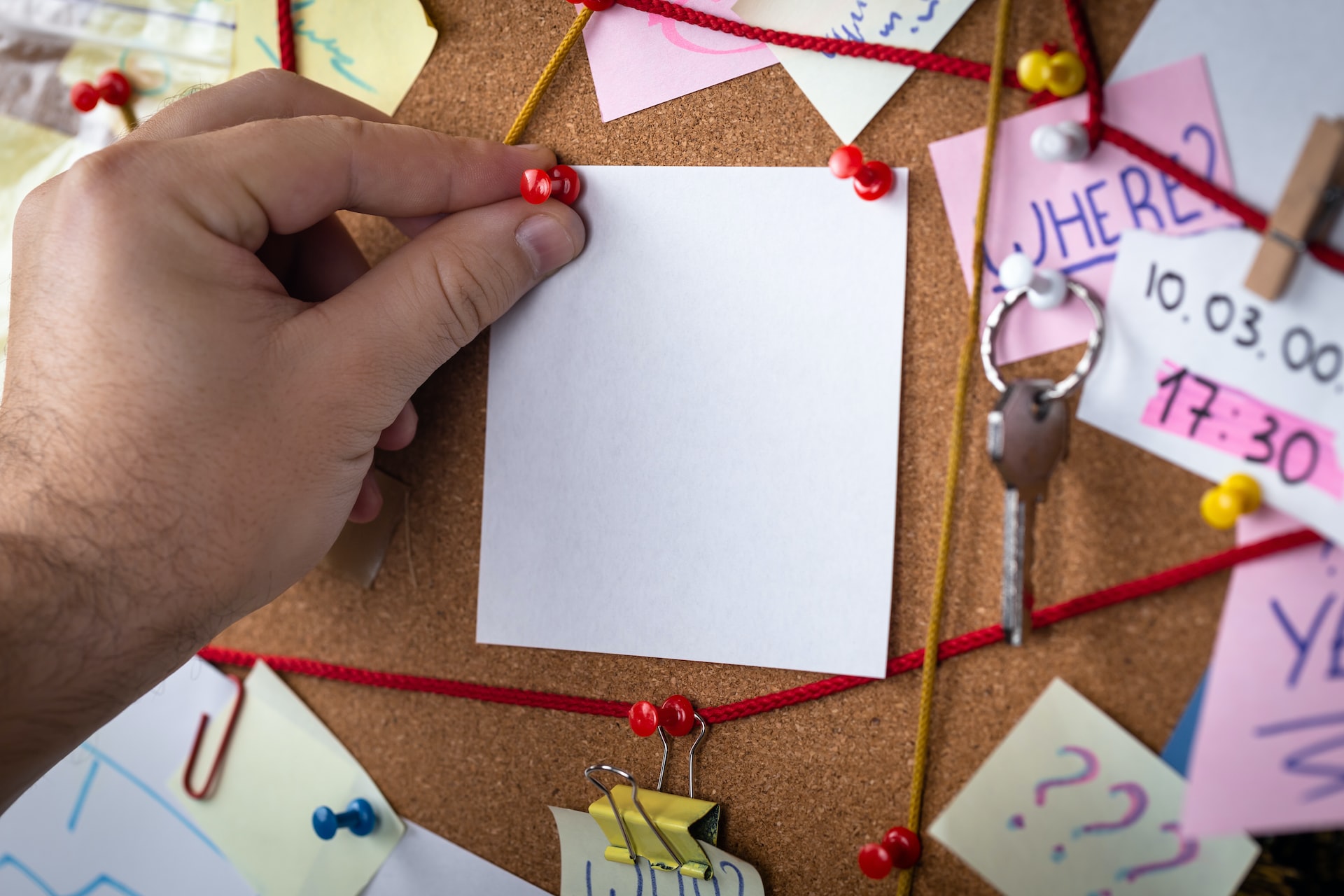 notes, pins, and string connected on a cork board